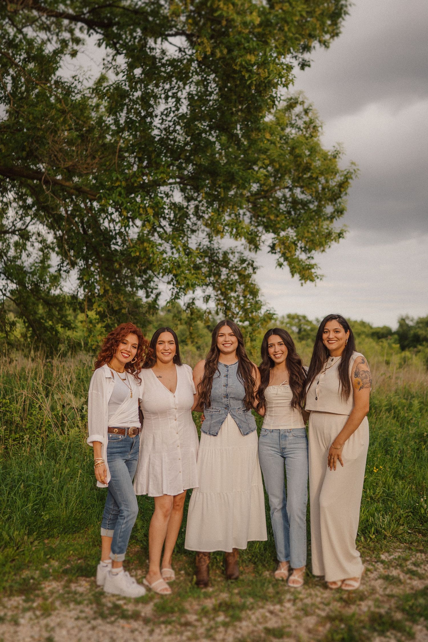A group of five people pose together outdoors wearing coordinated neutral-colored outfits.