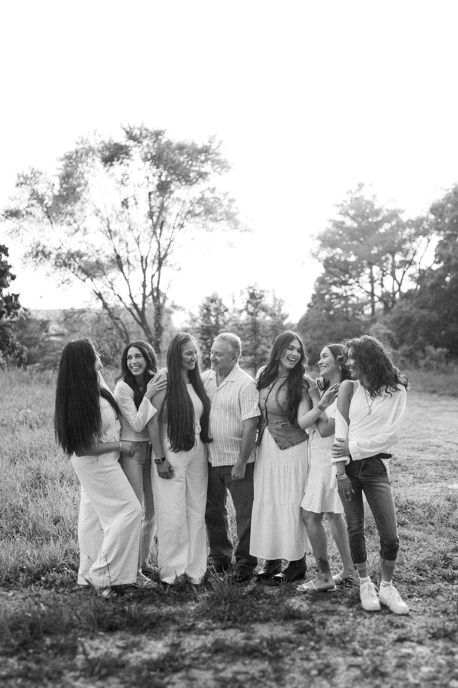 A black and white photo shows a group of people standing together and laughing in a casual outdoor setting.