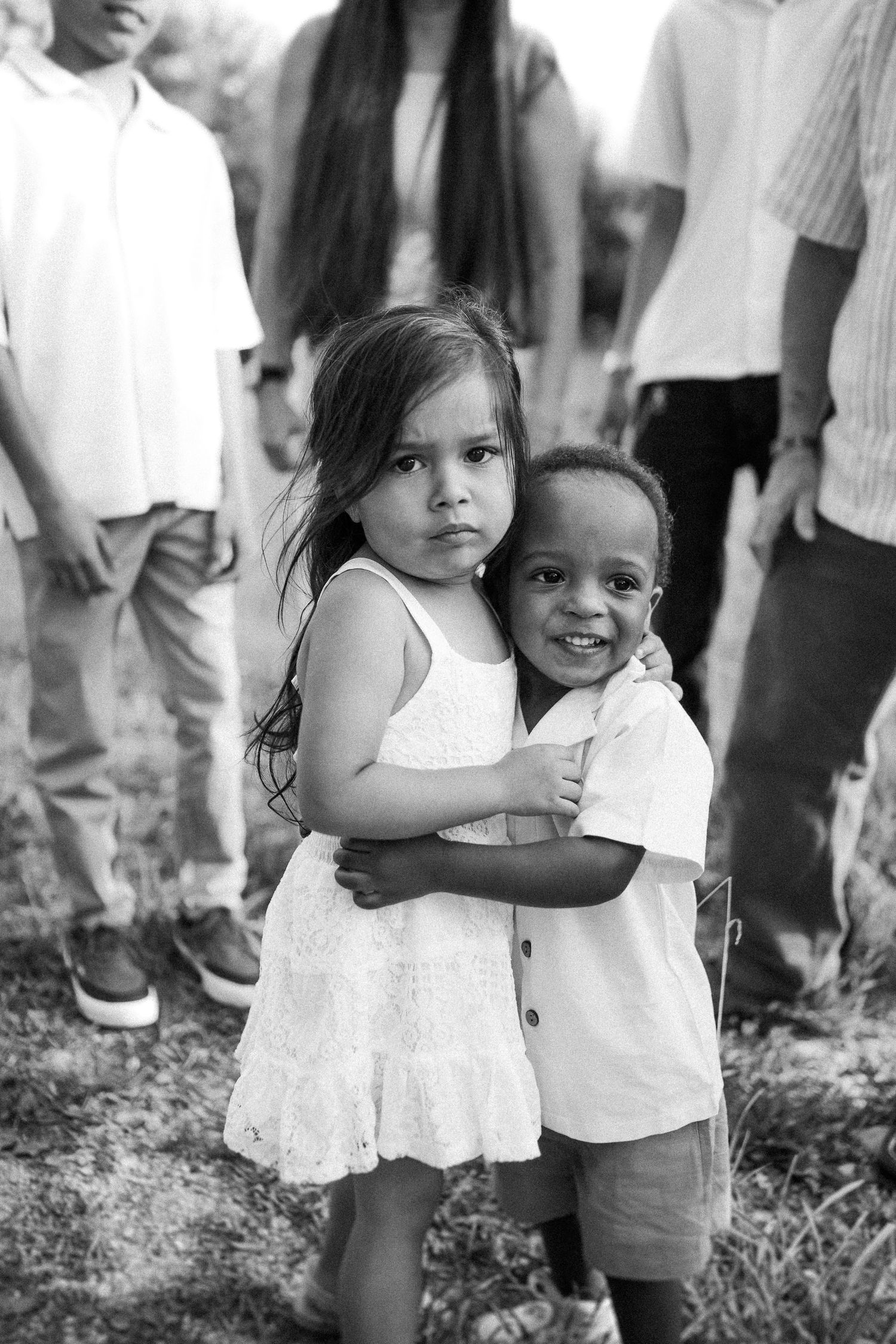 Children wearing white dresses play together in a black and white outdoor scene.
