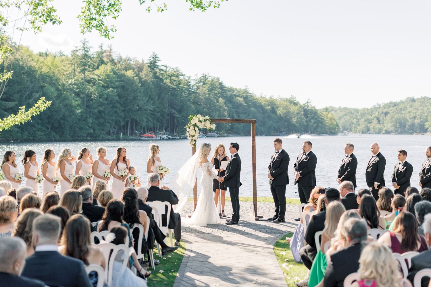 Outdoor wedding ceremony setup with white chairs along a path leading to waterfront venue at sunset.