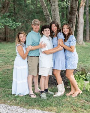Family photo session in a wooded setting with everyone wearing coordinated blue and white clothing.