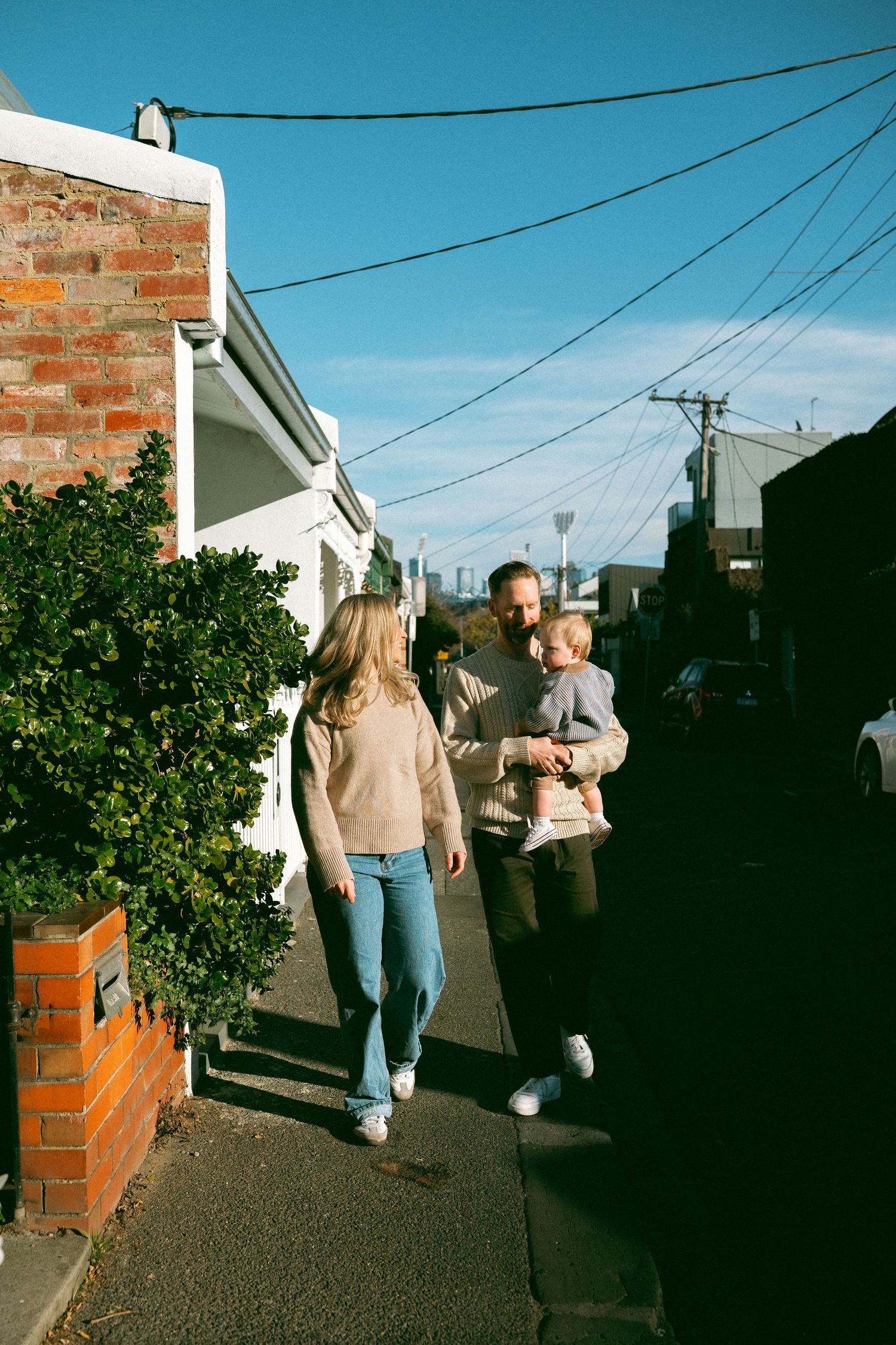 A family walking the streets of Richmond with the MCG in the background.