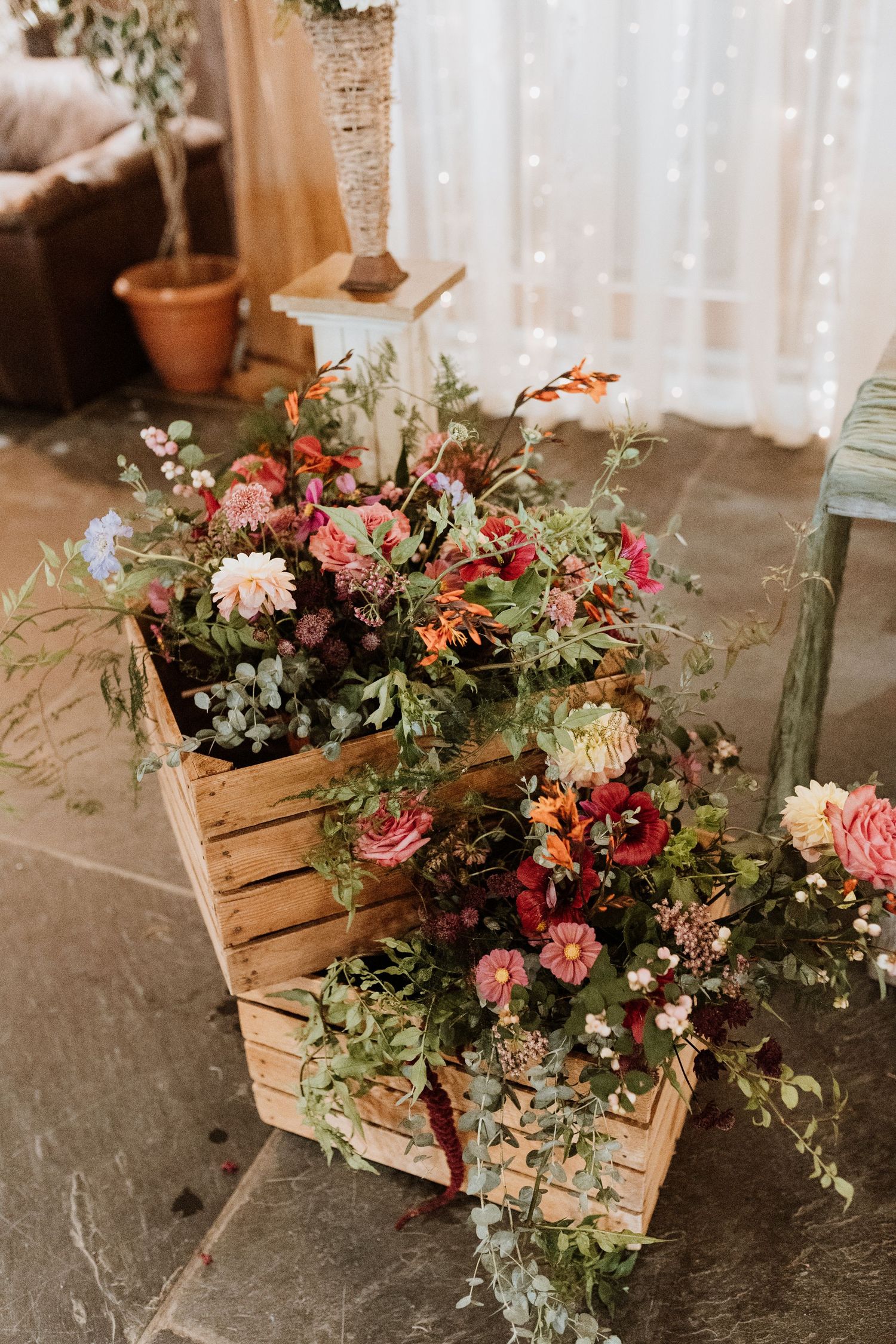 A two-tiered white wedding cake decorated with edible pansies sits on a wooden stand surrounded by floral cupcakes.