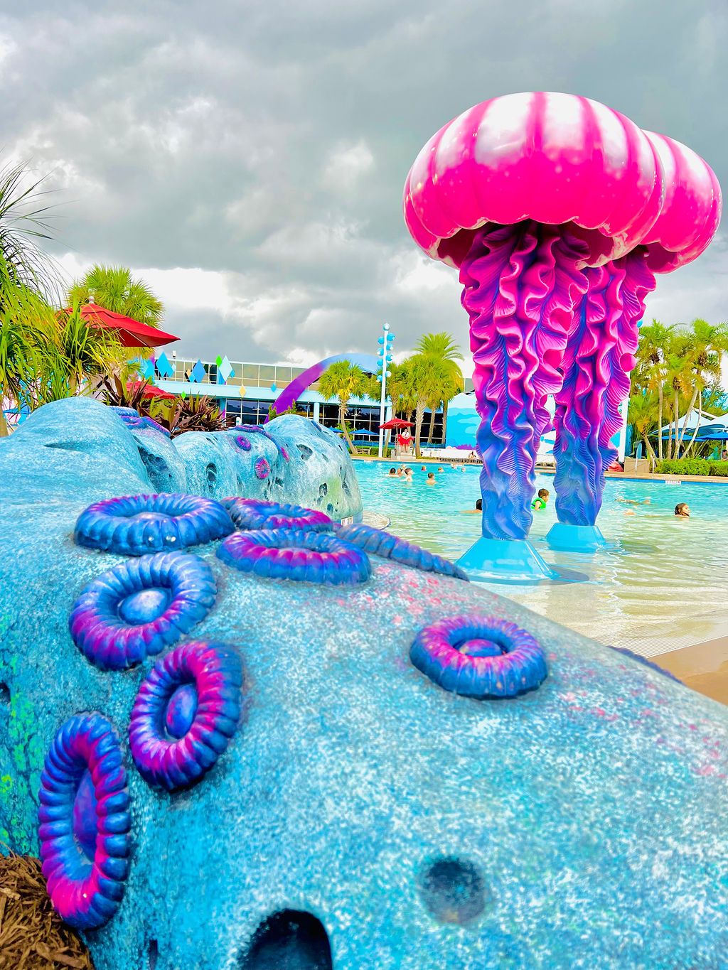 Vibrant pink and purple jellyfish sculpture in a themed pool area with blue decorative elements.