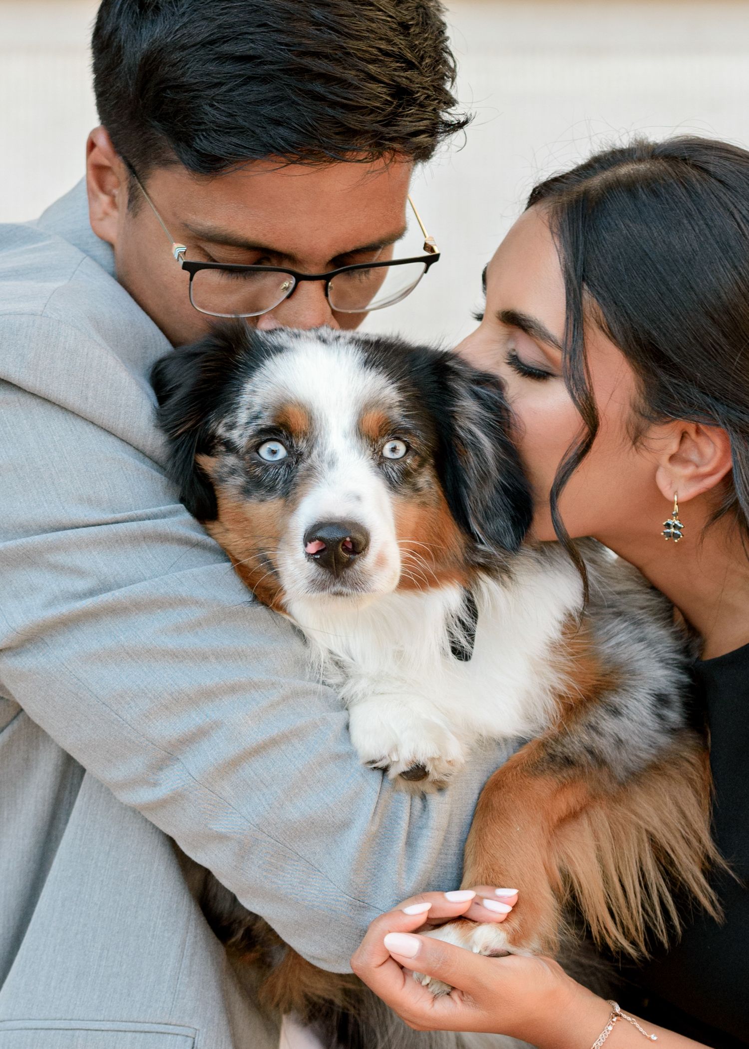 A couple hugs and kisses their Australian Shepherd dog who has striking blue eyes.