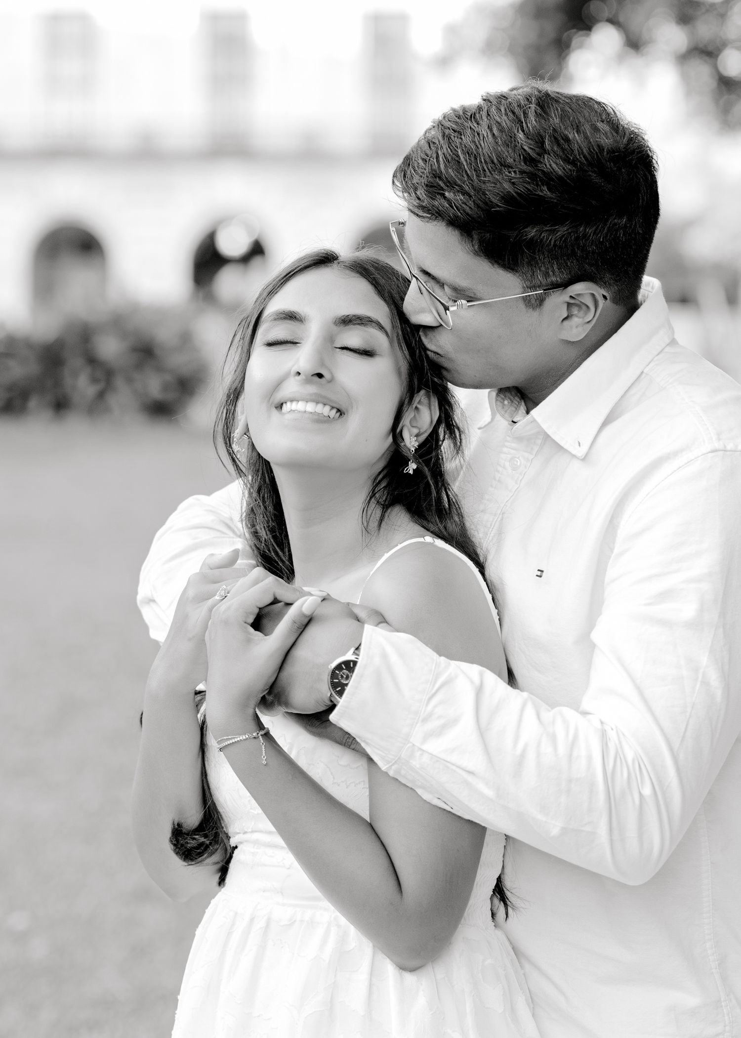 A couple shares a tender black and white moment outdoors as they embrace in romantic formal attire.