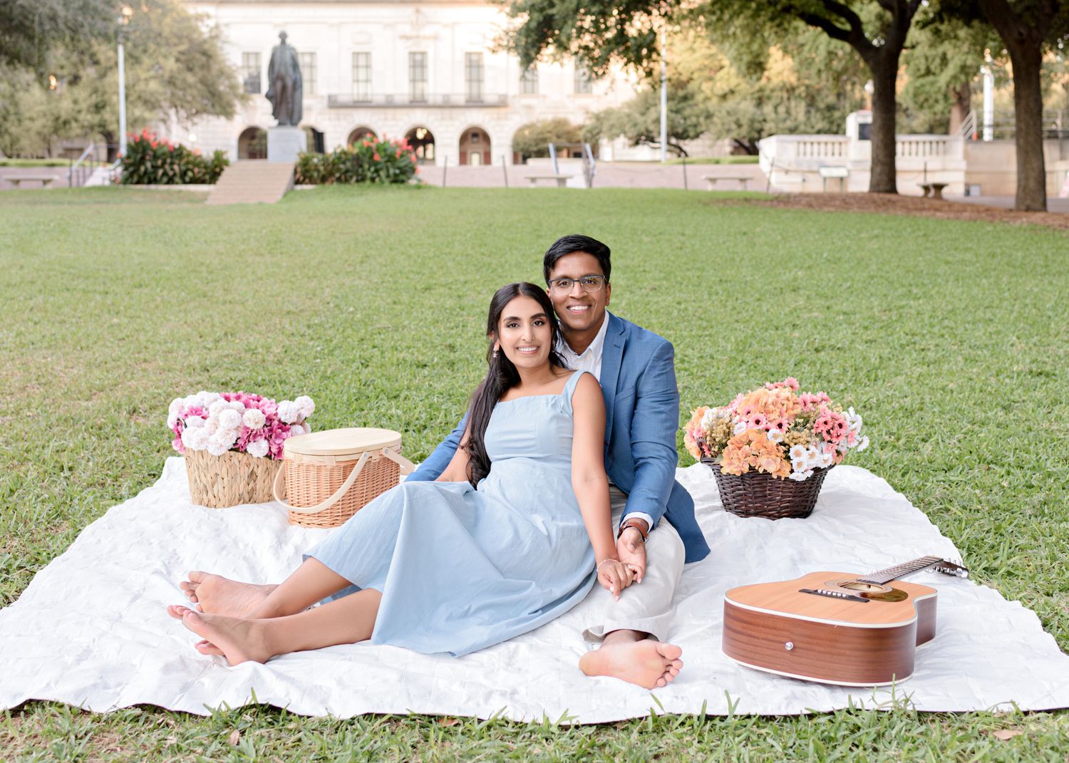 A special outdoor picnic scene on a white blanket with flower baskets and guitar on a grassy lawn.