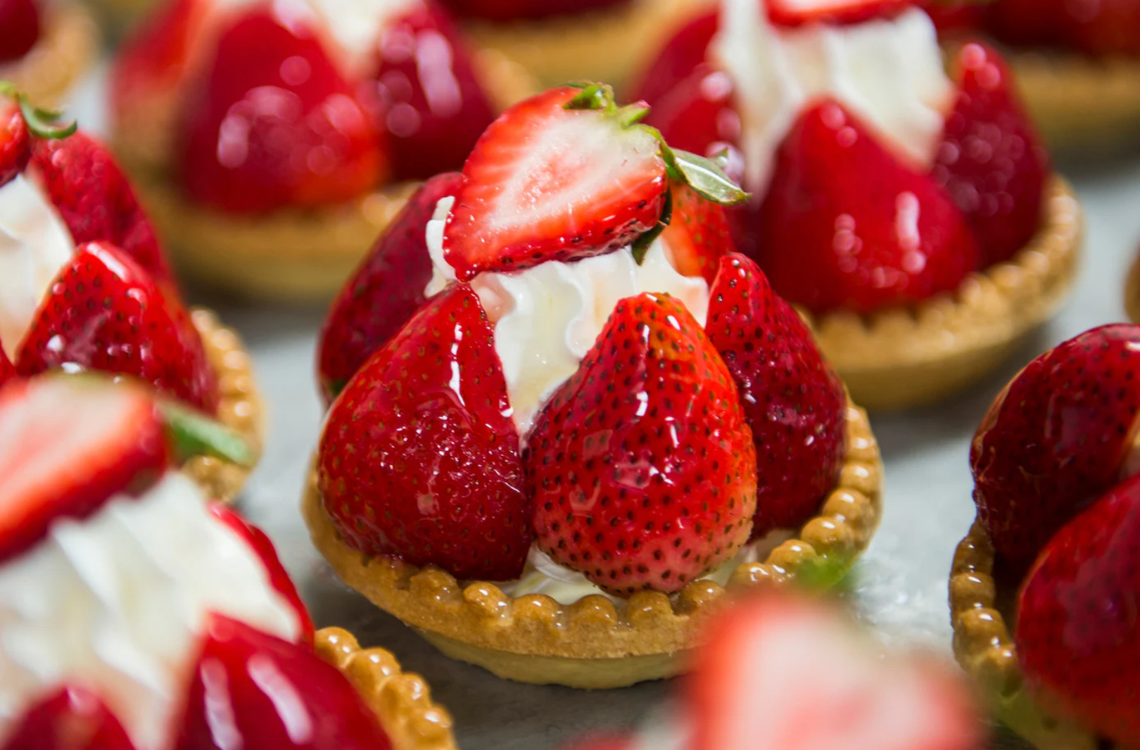 Fresh strawberry tarts with whipped cream arranged on a dessert platter.