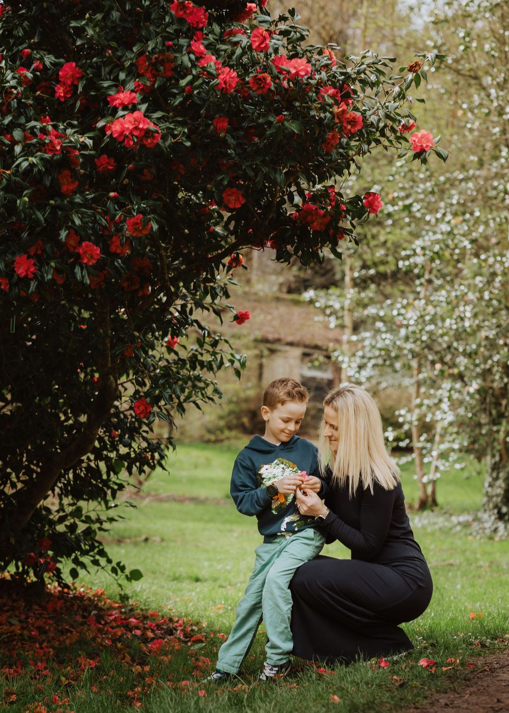 A tender moment shared beneath a vibrant red rose bush in a lush garden setting.