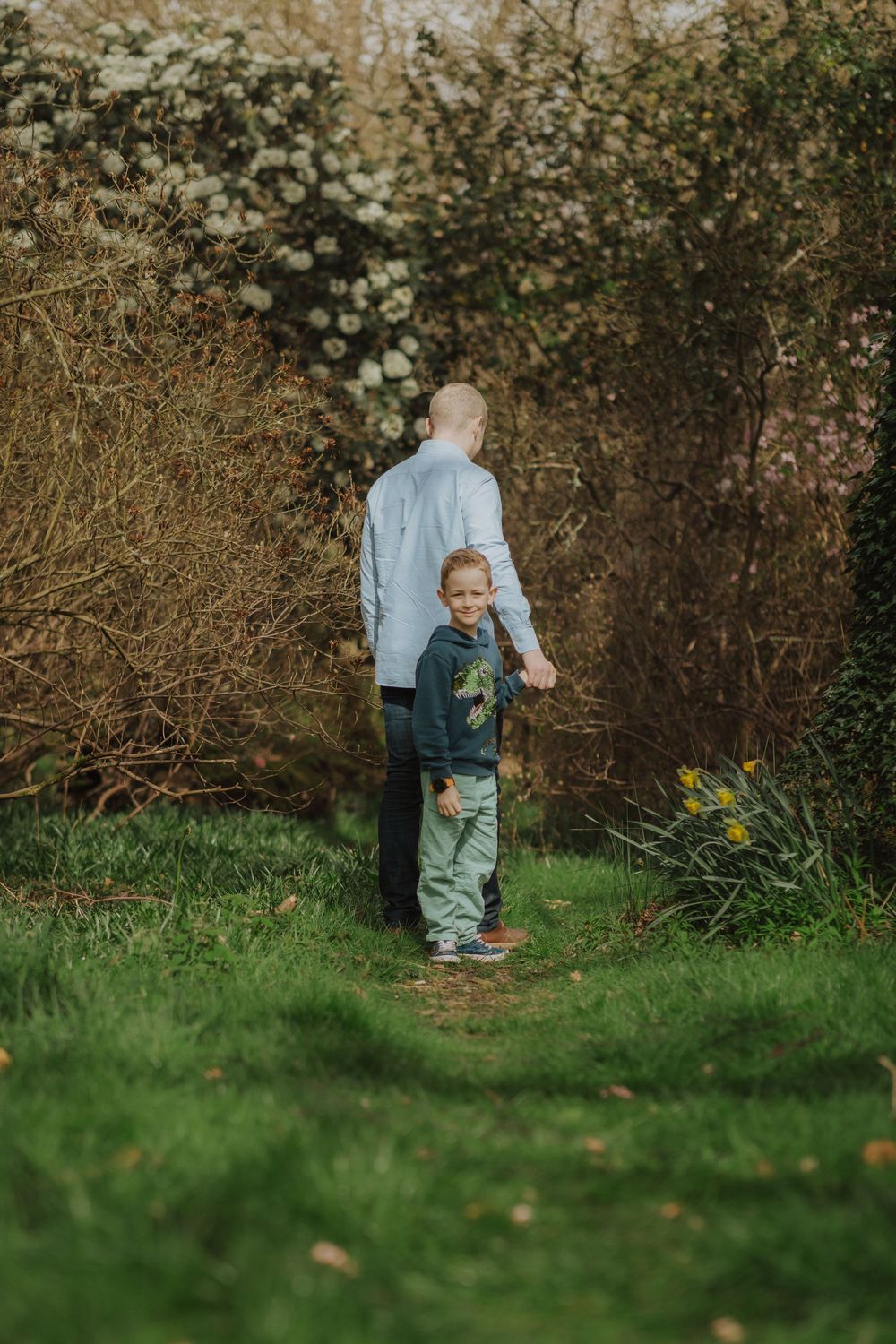 A toddler in winter clothing walks through a garden path while exploring the natural surroundings.