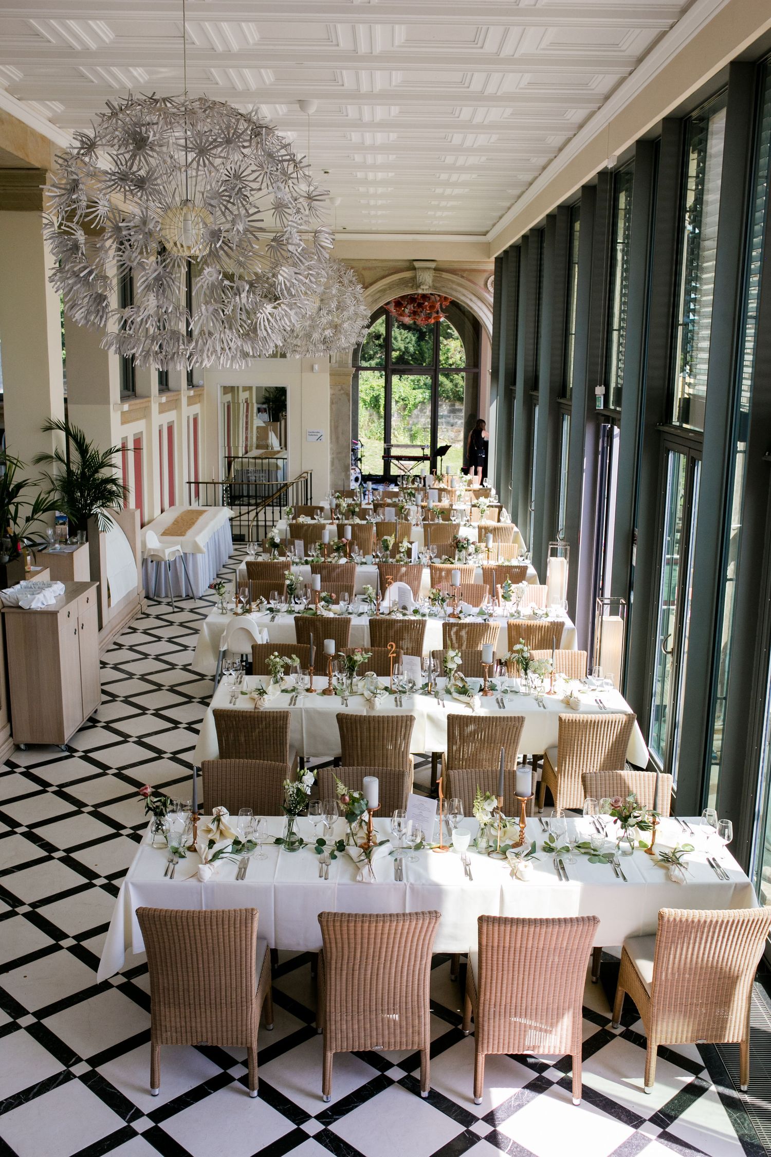 Elegant wedding reception hall with black and white checkered floor, glass walls, and round tables set for dinner service.