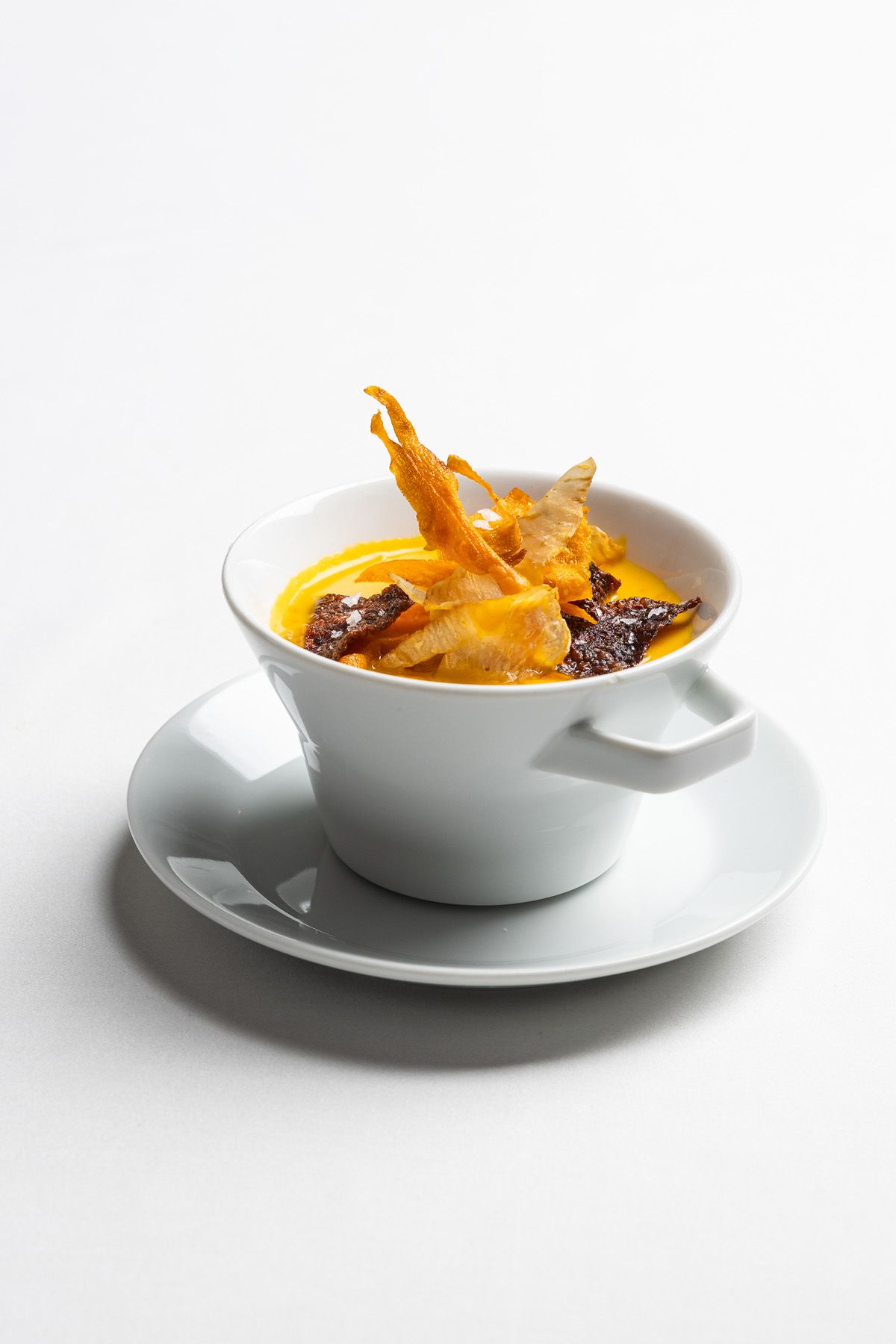 Coffee splashing dramatically from a white ceramic cup and saucer against a plain white background.