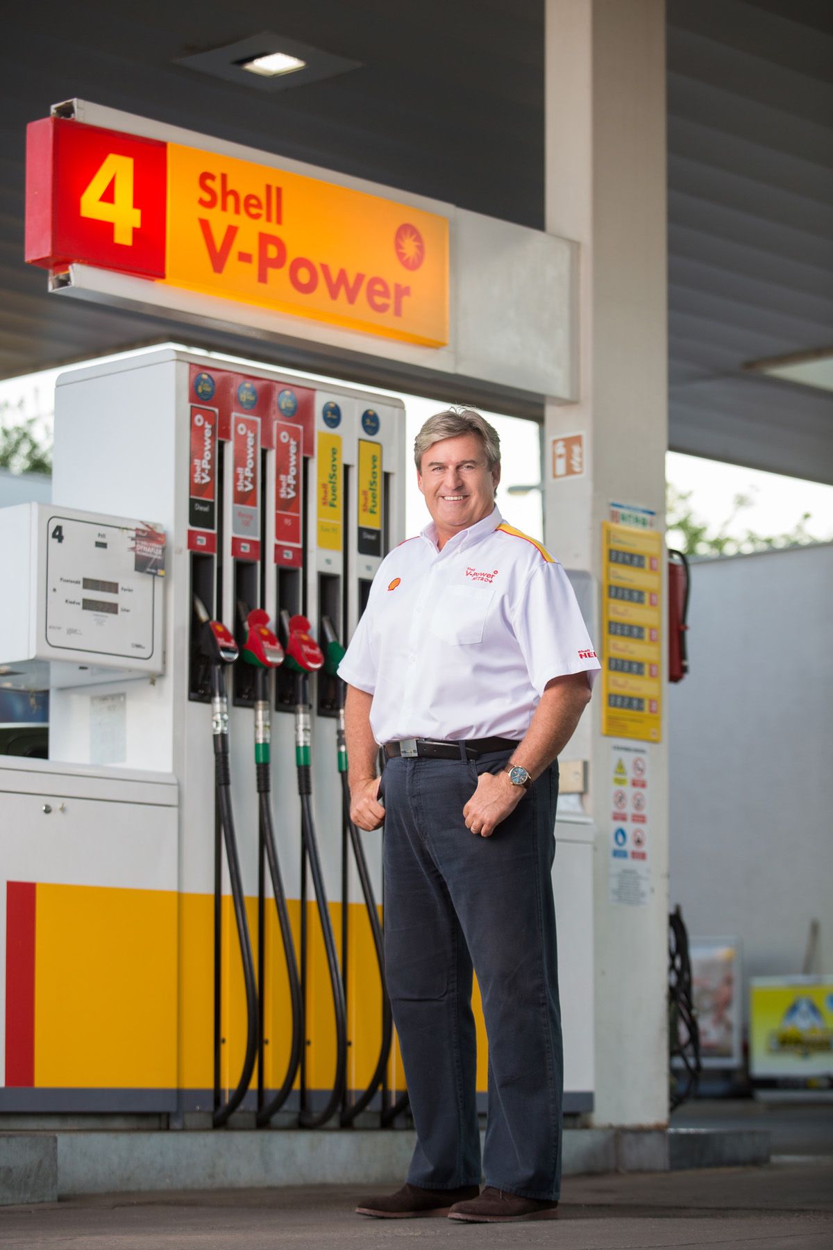 Shell gas station employee standing next to fuel pumps under yellow and red branded signage.
