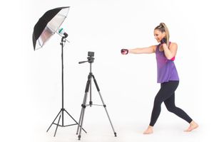 Woman in athletic wear exercising with resistance bands in a bright white studio setup with lighting equipment.