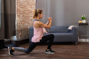 Person in pink tank top performing lunges during an indoor workout session in a room with exposed brick walls.