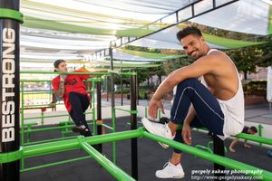 Athletic figures perform exercise movements using green suspension straps in an outdoor fitness area.