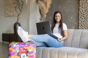A person sits on a gray couch showing off colorful sequin mermaid pillows in different decorative patterns.