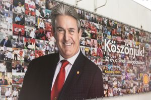 Professional business portrait displayed on wall with collage of photos and text reading Koszonto in background.