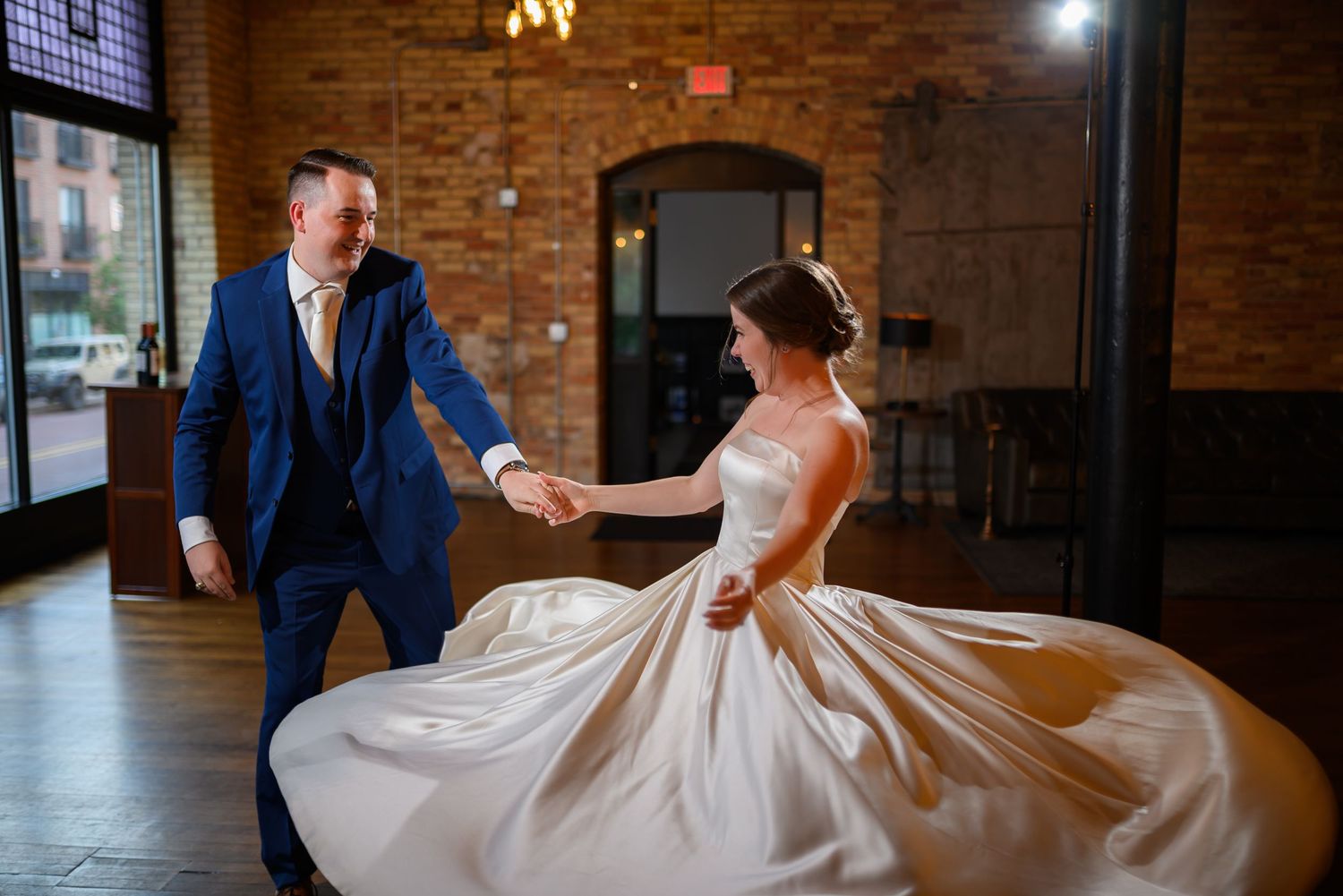 A bride in a flowing white gown twirls on a dance floor in The Rutledge against the brick-walled venue.