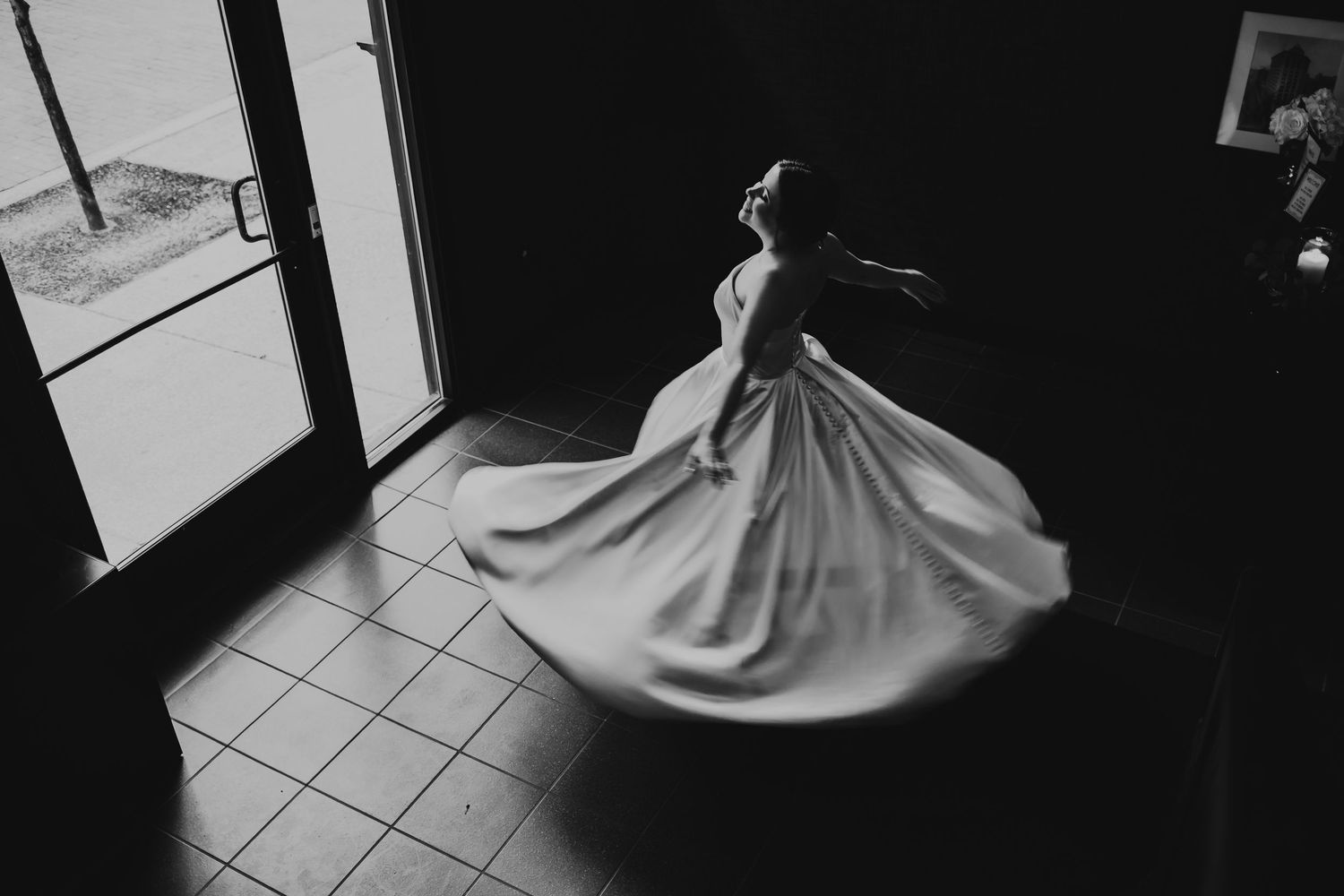 A dramatic black and white shot shows a flowing white wedding dress in motion against tiled flooring.