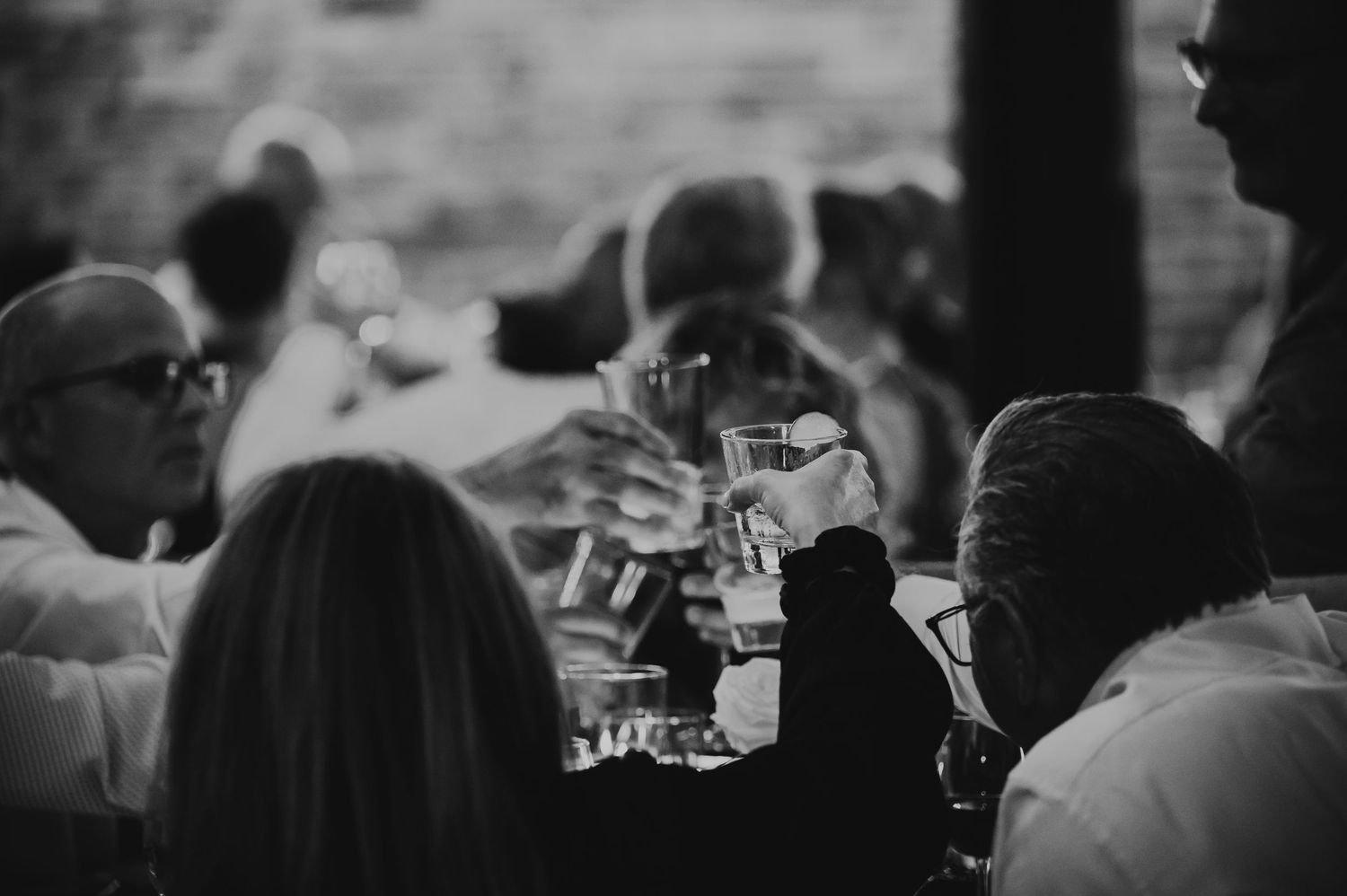 A black and white photo shows guests seated at a table with wine glasses during what appears to be a dinner event.