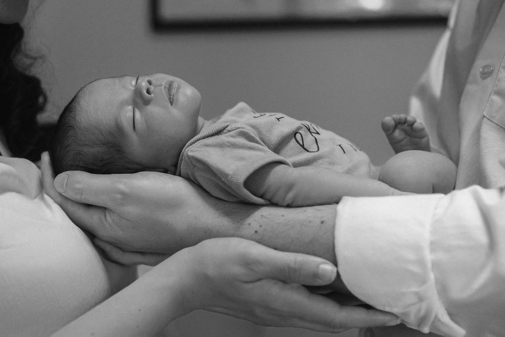 A tender black and white photo of a newborn baby girl lay in mother and fathers arms
