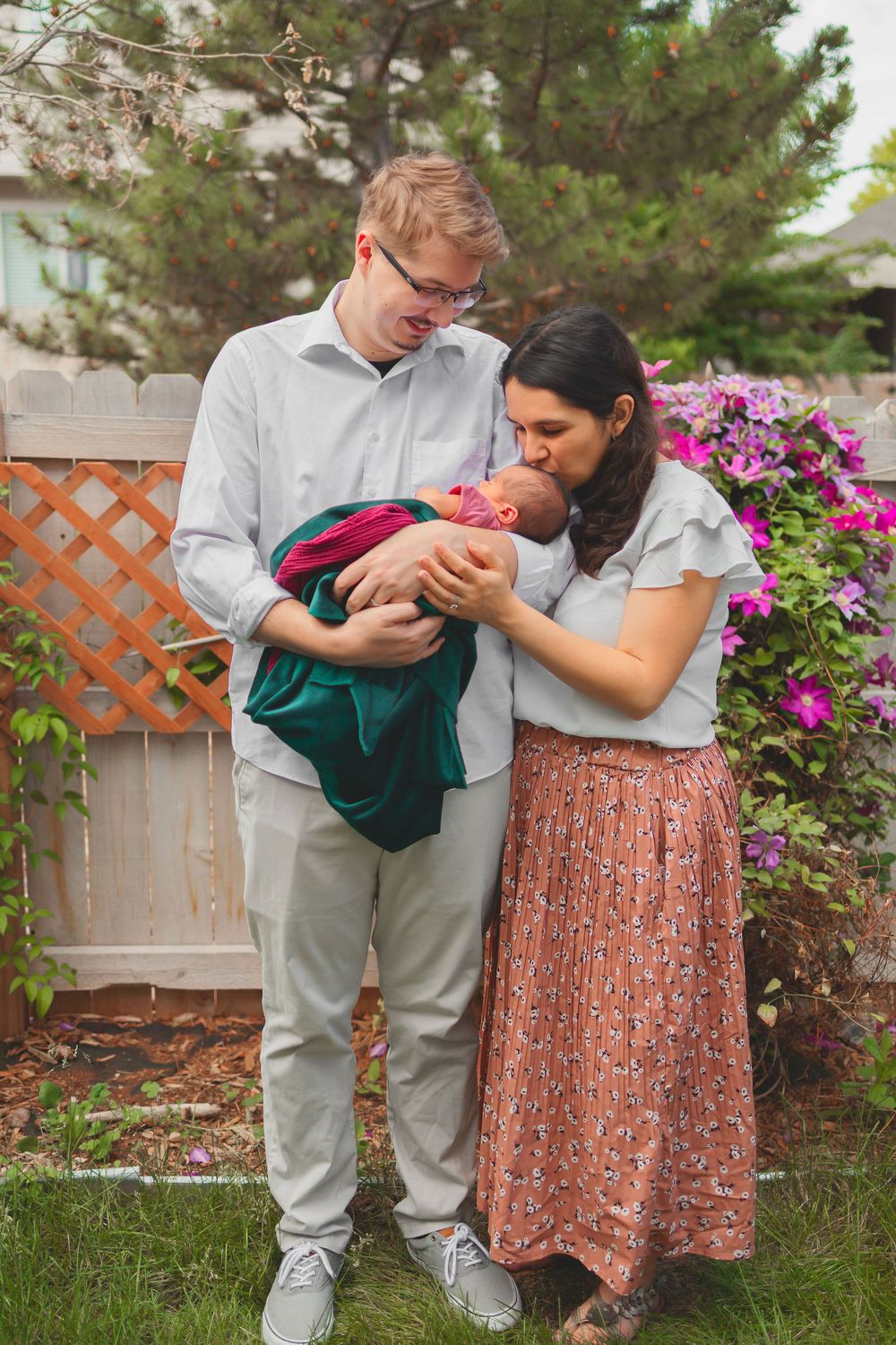 Mom and dad sharing a tender moment in a garden with blooming pink flowers and wooden fence in the background.