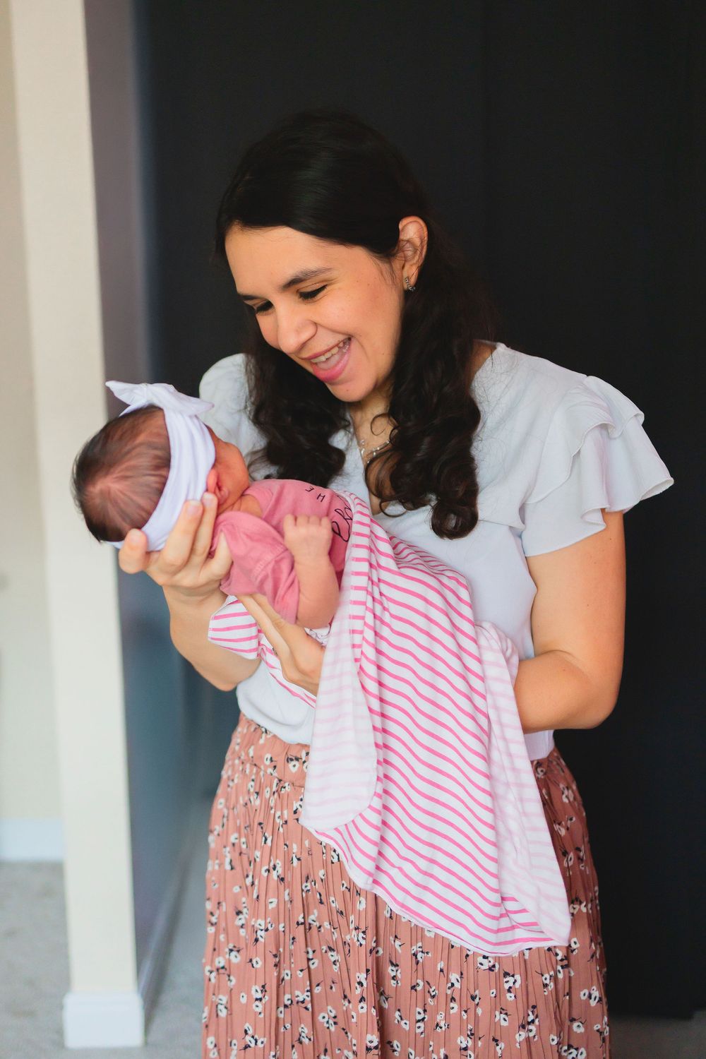 A person in a floral dress stands indoors holding A NEWBORN BABY GIRL