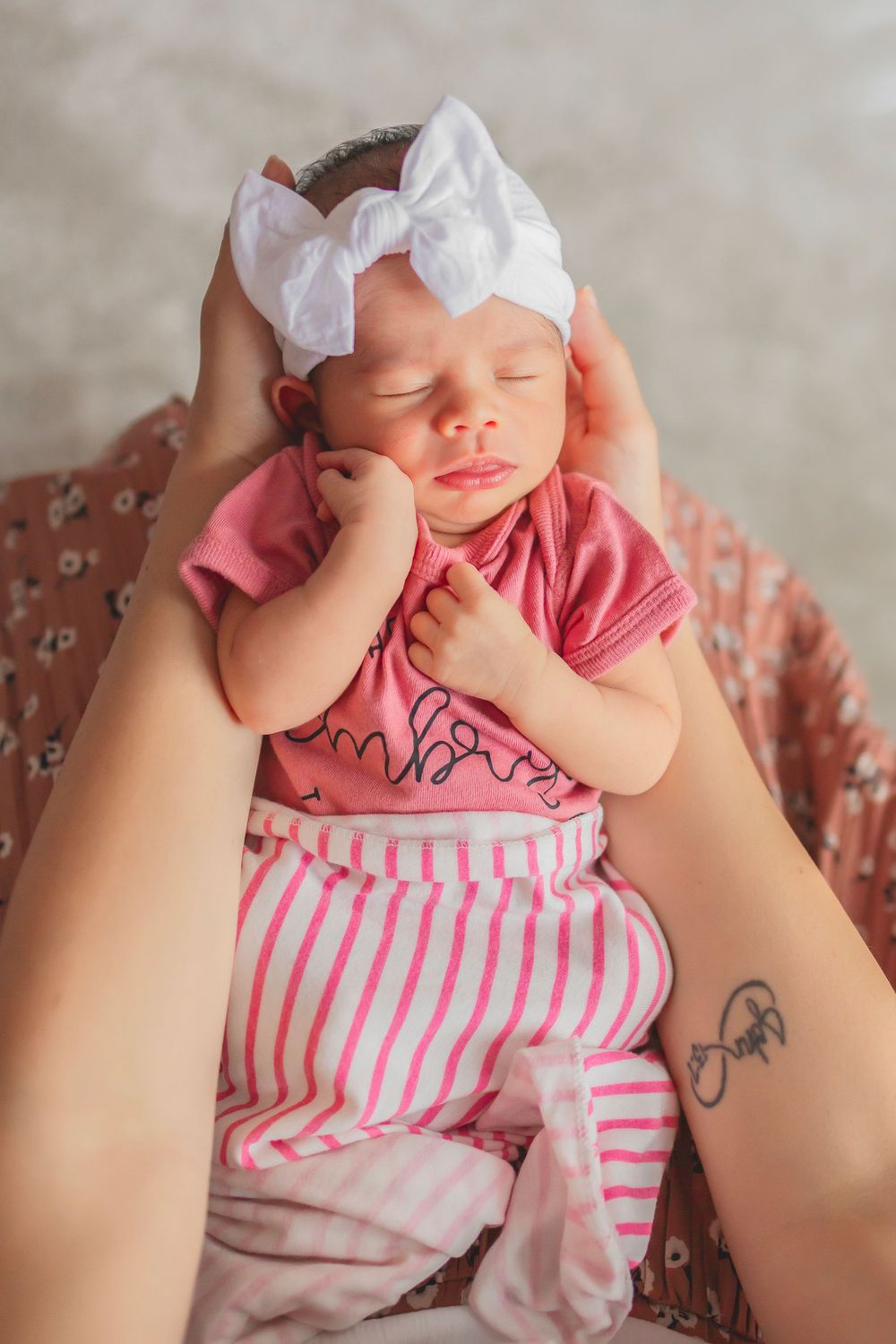 A sleeping baby wearing pink and white striped clothing rests peacefully with a white bow headband.