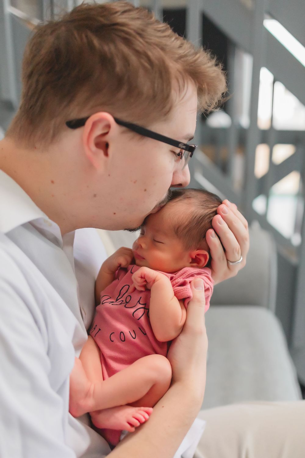 A tender moment between Dad and baby in pink onesie.  He is holding baby up and kissing her head