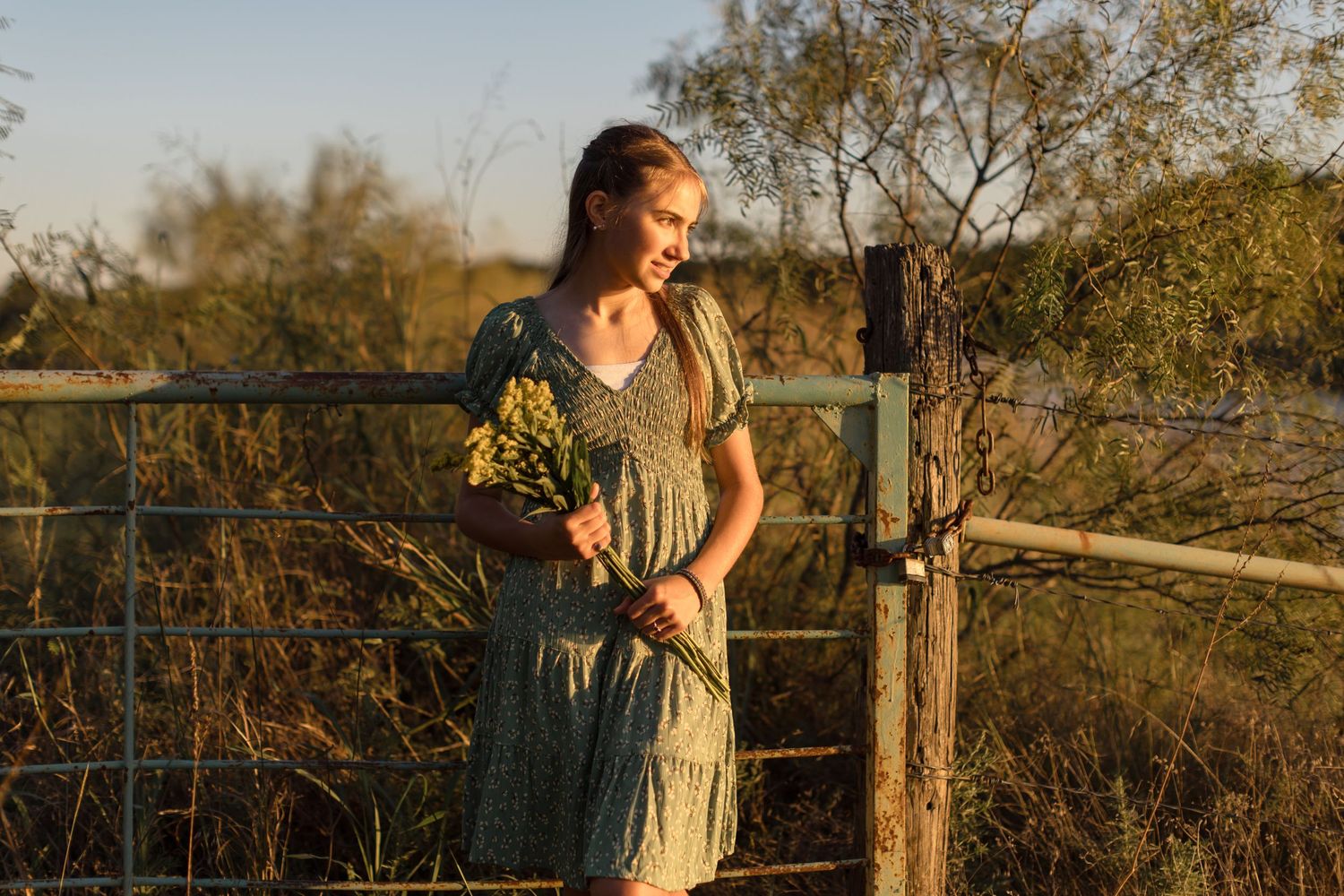 Golden sunset light illuminates a rustic wooden fence and natural landscape for this senior girl.