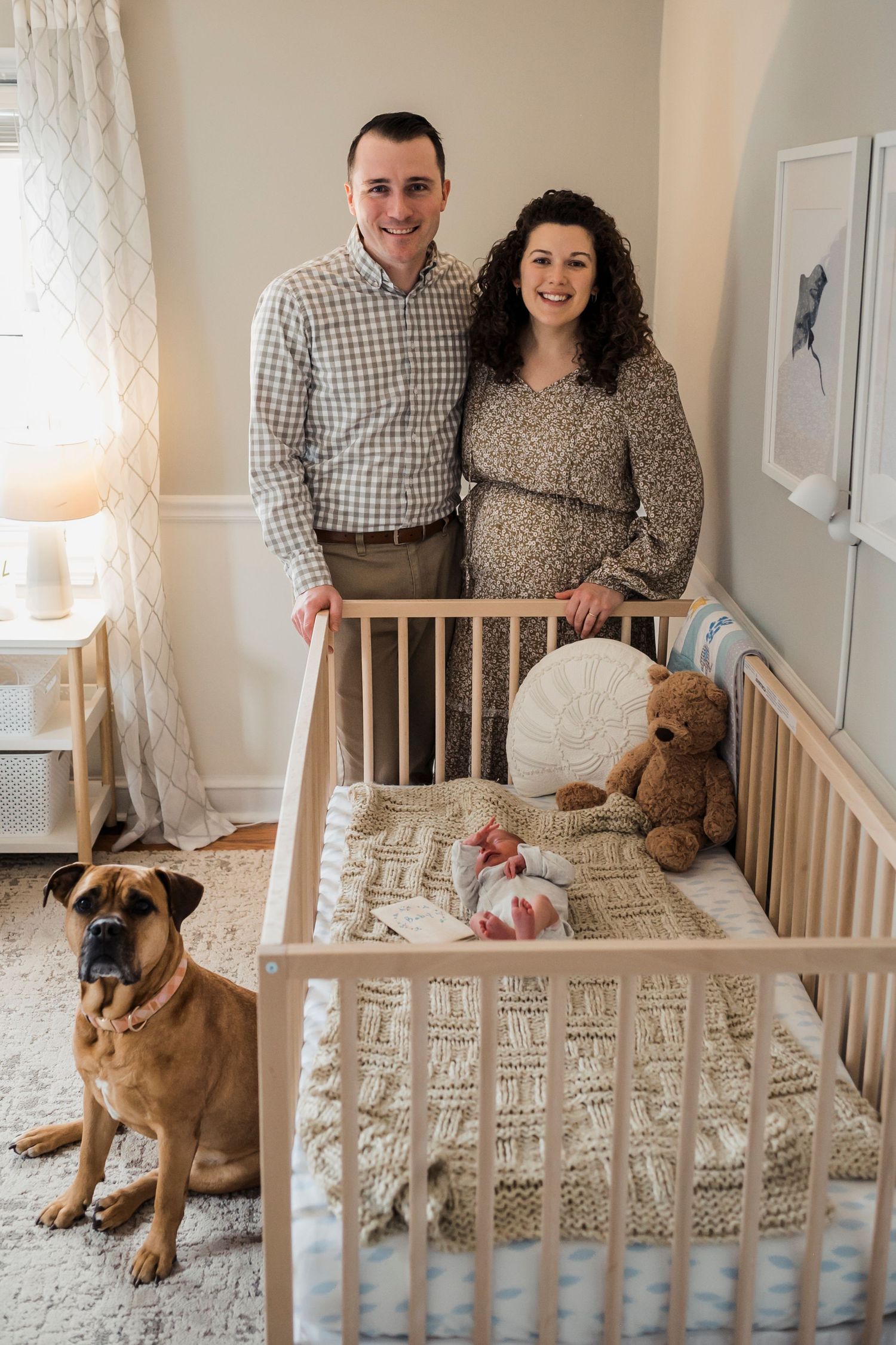 A nursery room with a wooden crib, stuffed animals, and a brown dog sitting beside two people.