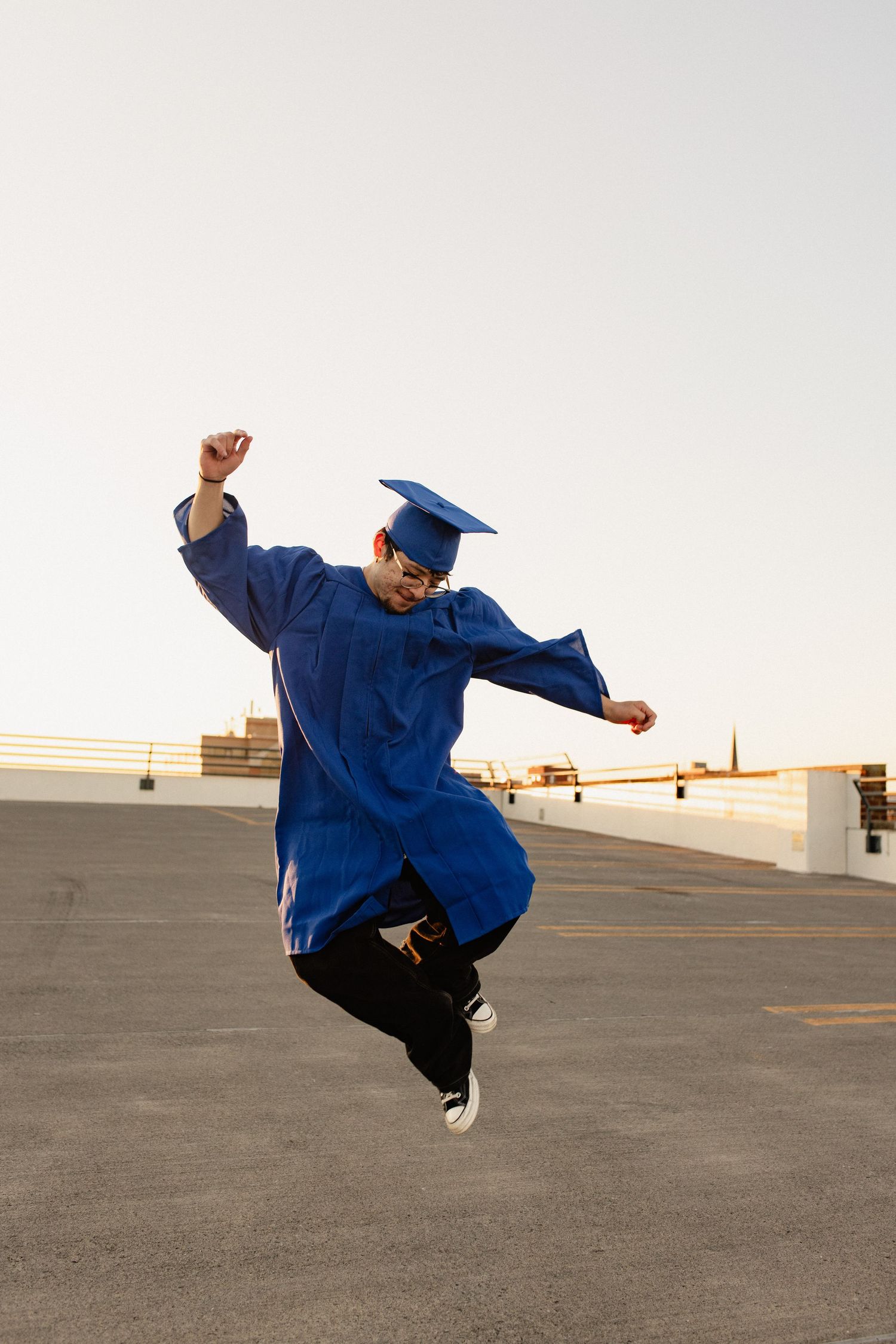 Person in blue graduation gown performs dynamic jumping poses against concrete backdrop in Frederick Maryland