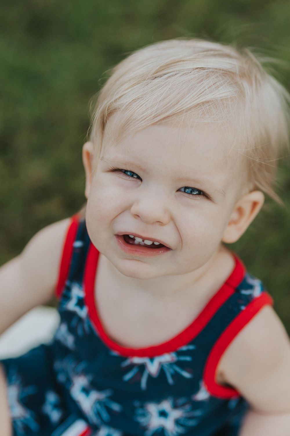 A smiling toddler in a navy and red star-patterned tank top poses outdoors.
