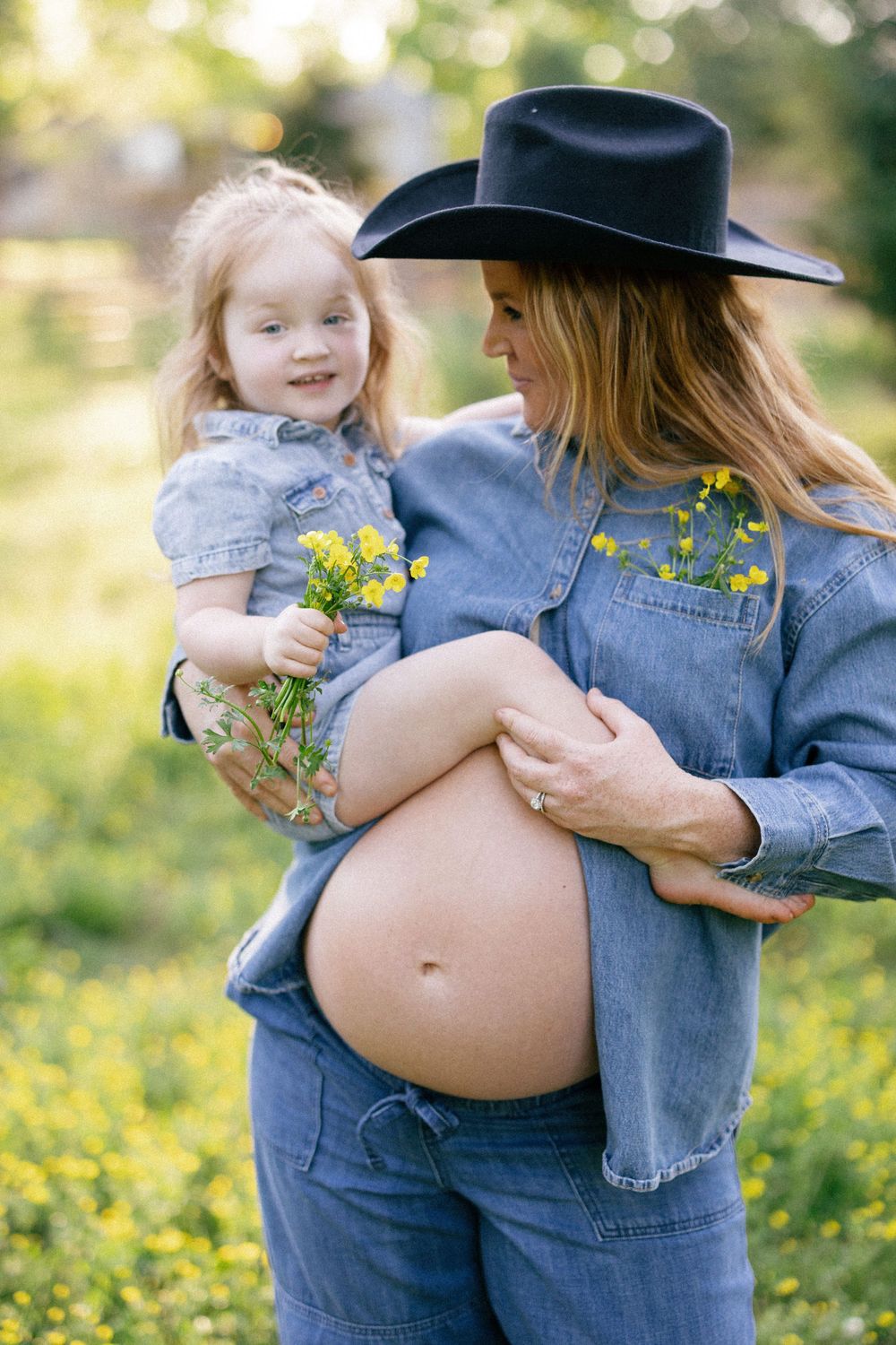 A tender family maternity moment captured in a field of yellow wildflowers on a sunny spring day.