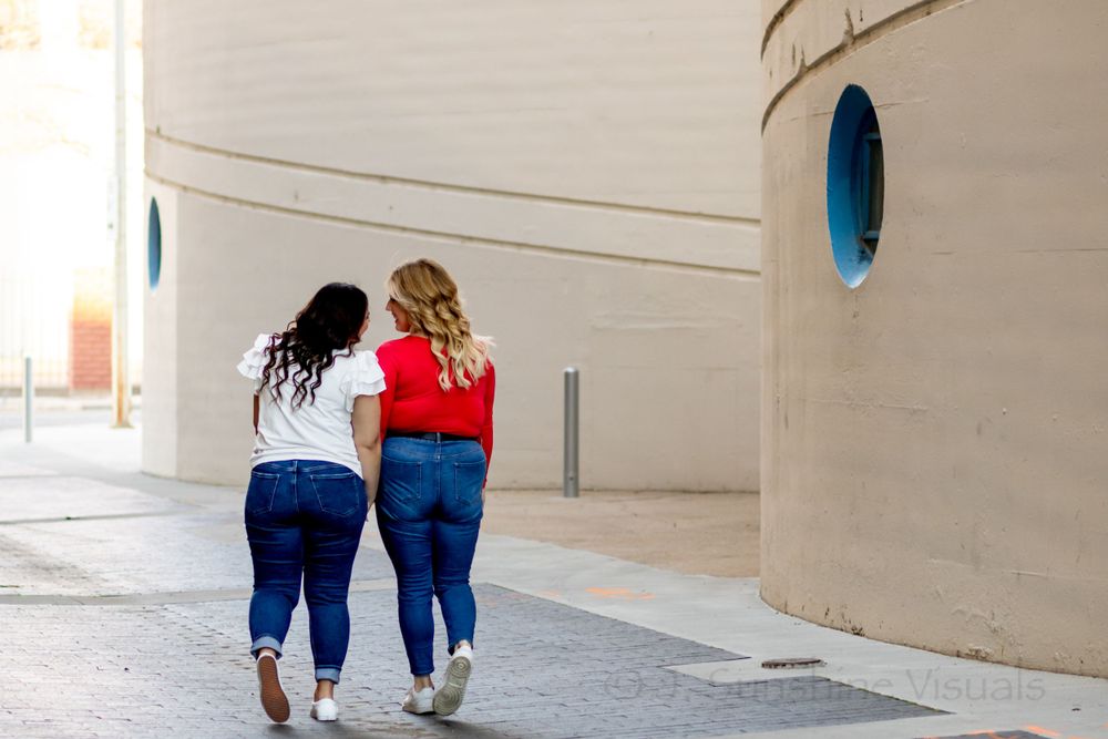 Two women in casual denim outfits walking together down a covered outdoor walkway with oval windows.