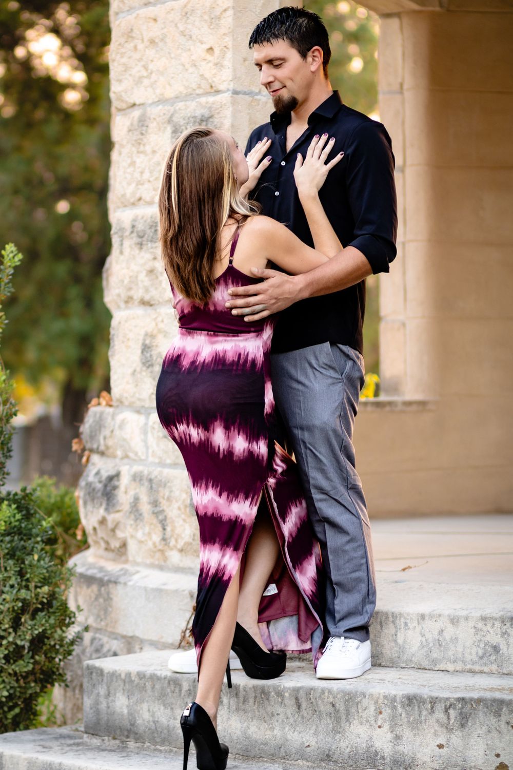 A romantic couple embraces on stone steps, with her wearing a striking purple tie-dye maxi dress and high heels.