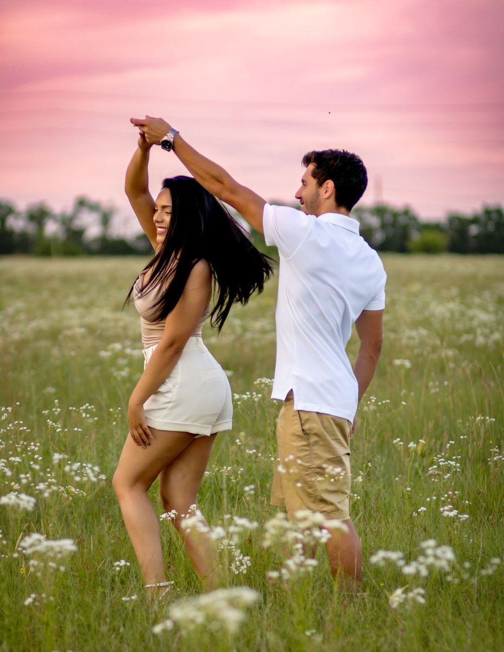 A couple dancing together in a wildflower meadow at sunset, creating a romantic silhouette against the pink sky.
