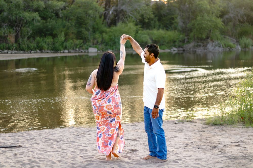 A couple dances together on a sandy beach by a serene lake during golden hour.
