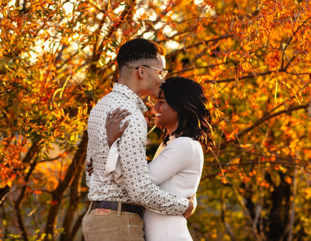 A couple embraces tenderly against a backdrop of vibrant autumn foliage with golden orange leaves in the background.