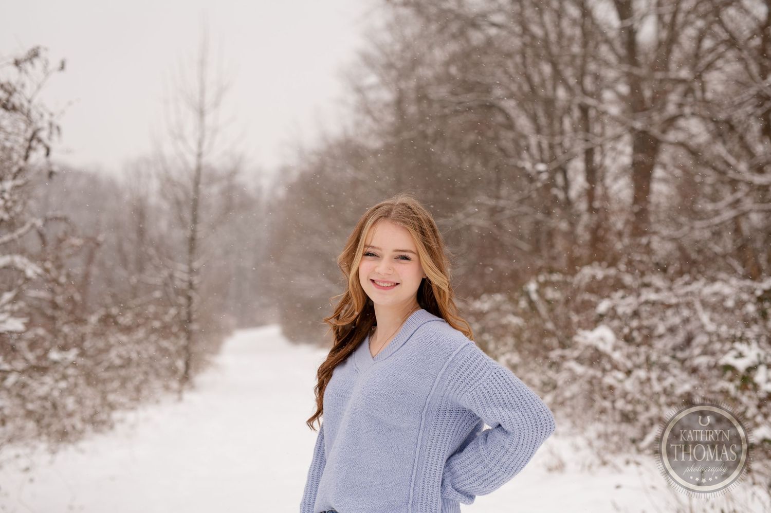 Person in light blue sweater poses outdoors in snowy winter landscape.