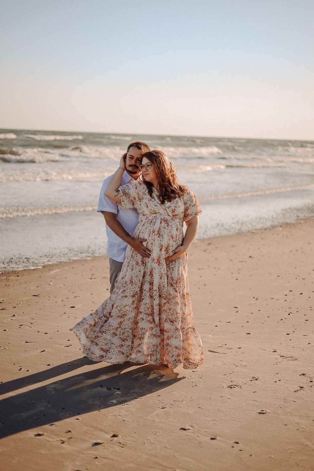 Sunset beach maternity photography in Eastern NC — couple embracing with ocean waves behind them.