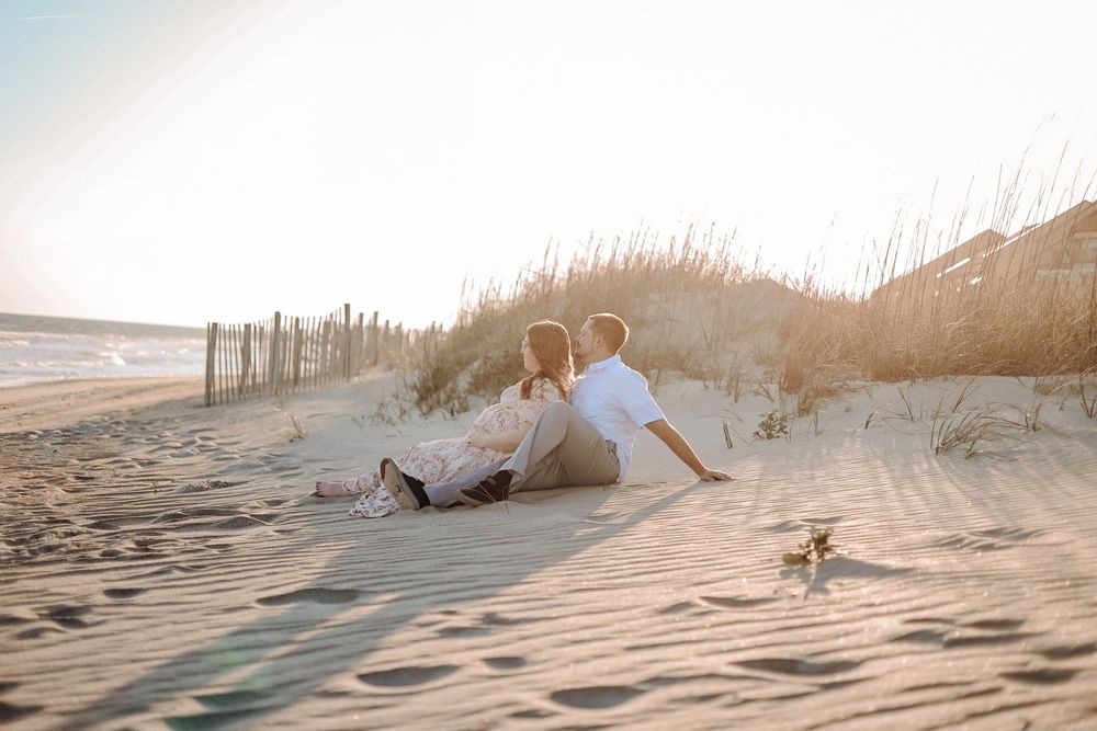 Couple sitting in the dunes during a sunset beach maternity session in Havelock NC, captured by Rosey Willow Photography.