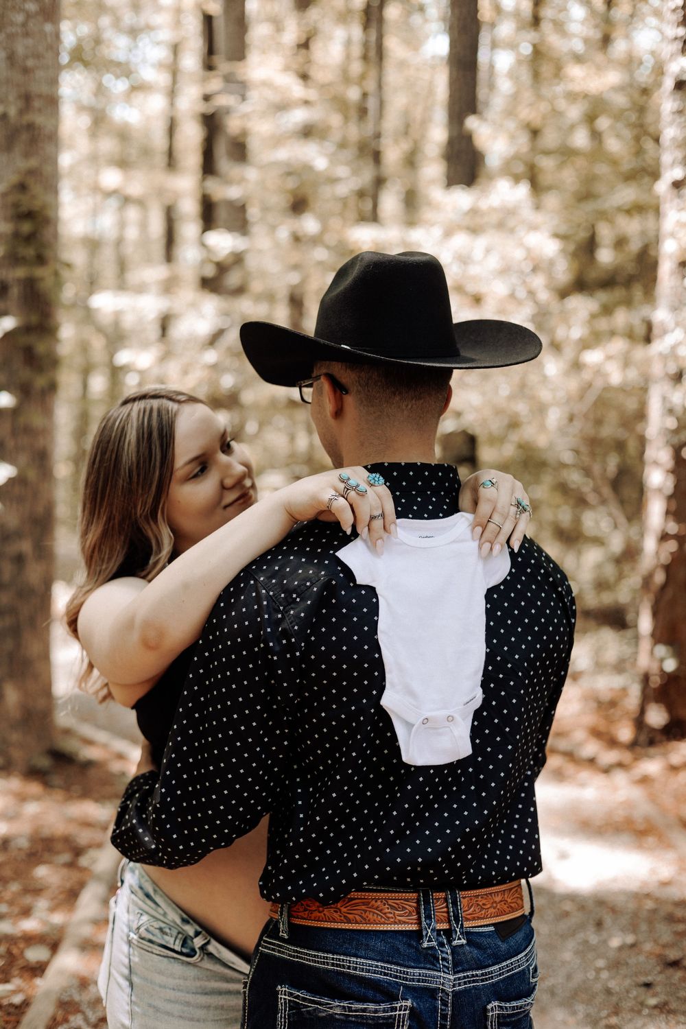 Pregnancy announcement photo — couple holding a baby onesie during a rustic forest maternity session in North Carolina.