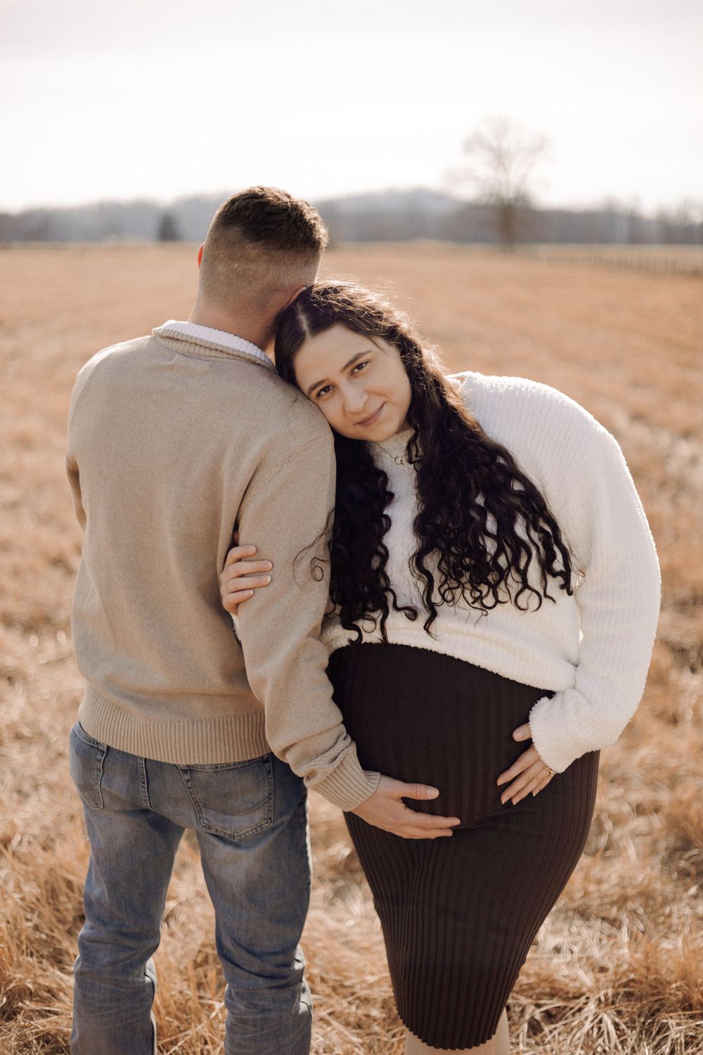 Intimate maternity portrait in rustic field with soft autumn lighting.