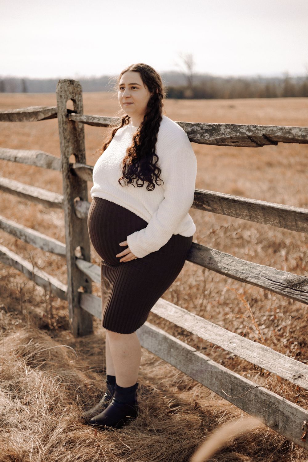 Maternity portrait against wooden fence in countryside setting.