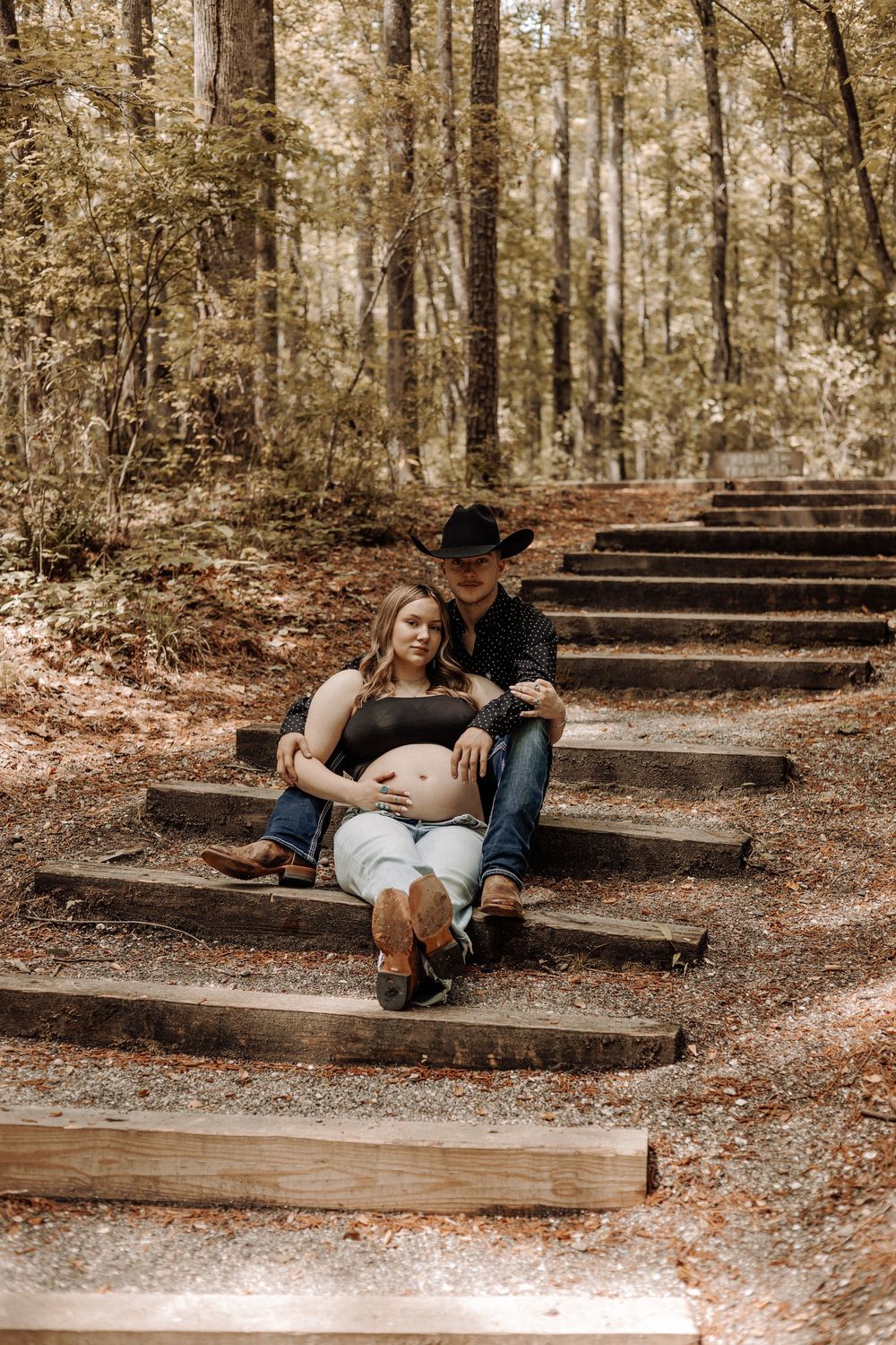 Outdoor maternity photography in Eastern NC — couple sitting on wooden steps in a sunlit forest.