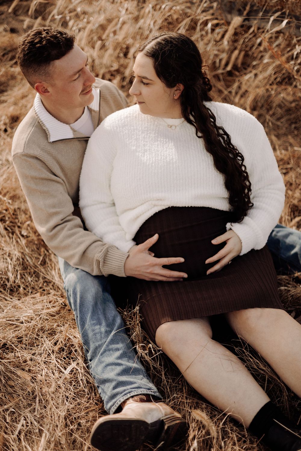 Couple sharing an intimate moment in a field of dried grass during maternity photoshoot.