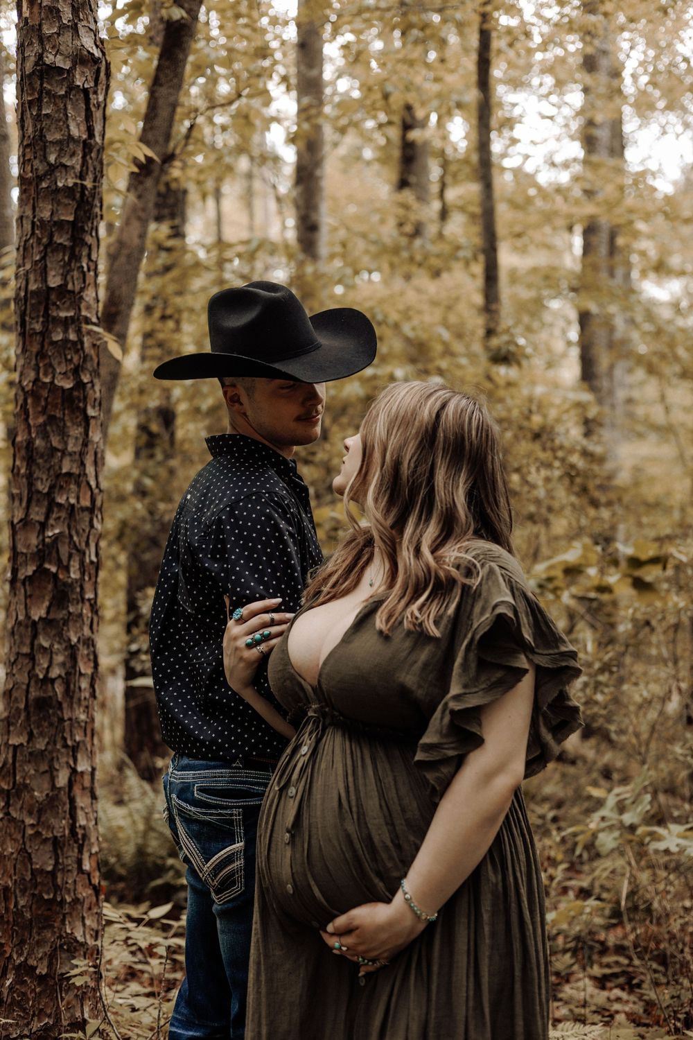 Western-style outdoor maternity session in North Carolina — couple embracing in a forest clearing at golden sunset.