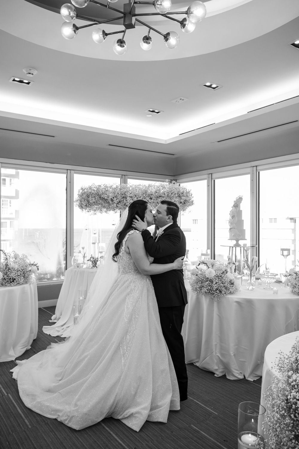 A romantic black and white wedding photo under a modern chandelier in an elegant reception space.